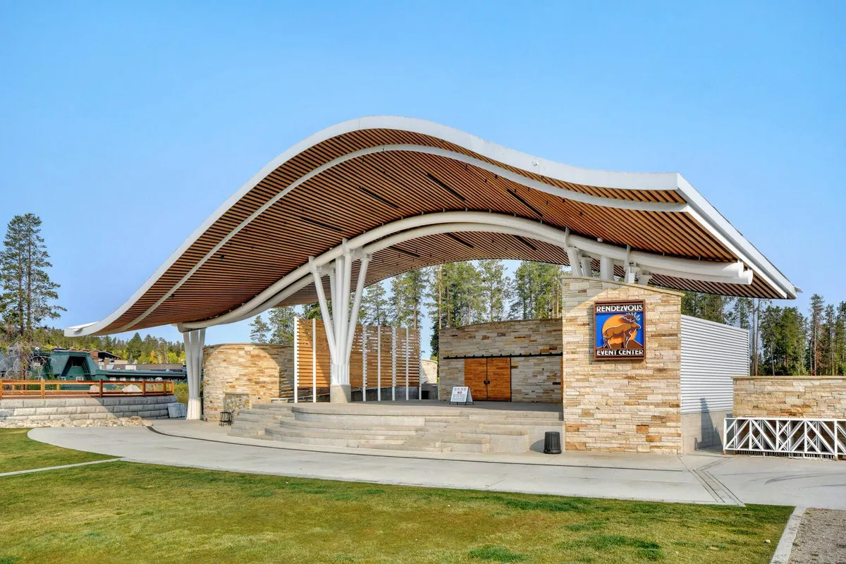 An exterior shot of the Hideaway Park amphitheater, showcasing its curved roof, stone walls, and steps leading to the stage. The venue radiates a sense of community and cultural excitement.