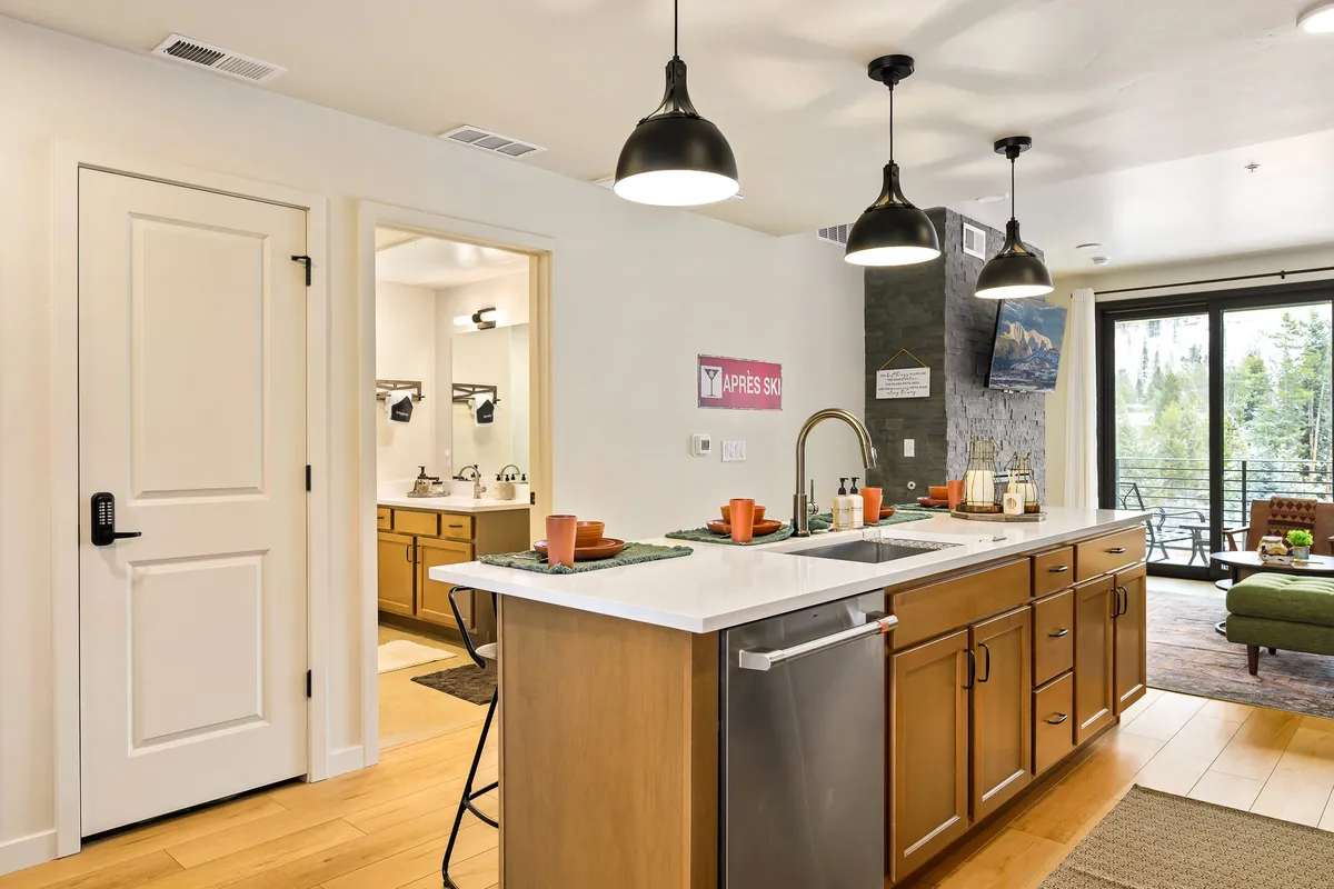 A wide-angle interior view connecting the kitchen island, dining table, pantry door, and a glimpse into the living area with views beyond. Modern finishes and a cozy setup invite guests to cook, dine, and relax while soaking in the serene ambiance and mountain vistas.