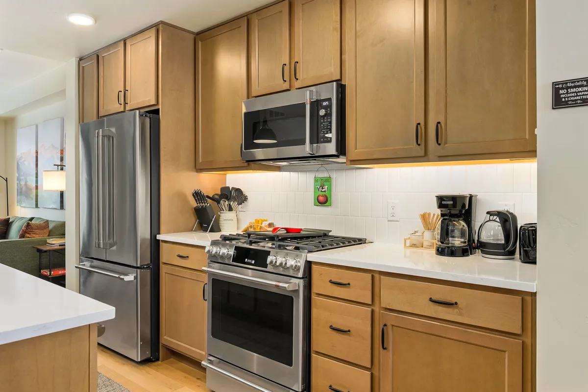 A modern kitchen equipped with stainless steel appliances, a white countertop, kitchen utensils, and a coffee maker. The space is bright, functional, and inviting, suggesting eco-friendly, high-end comfort where guests can prepare meals with ease.