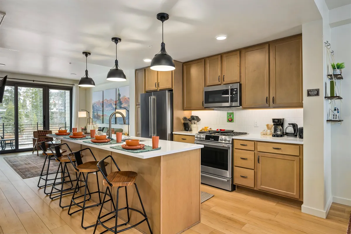The image showcases a bright and modern kitchen with an inviting island counter, high-end appliances, a stylish dining setup, and expansive windows that flood the space with natural light. The scene feels warm and welcoming, perfect for gatherings, holiday feasts, or sipping morning coffee while taking in the stunning surroundings of Winter Park.